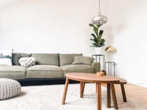 Eine gemütliche Wohnzimmeransicht mit warmem Licht, stilvoll eingerichtet und harmonisch inszeniert mit Beistelltischen aus Holz und Couch in Khaki von Raumgestaltung Gruber.