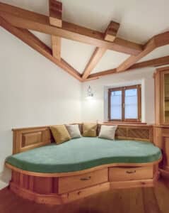 Neupolsterung für eine Couch bzw. Tagesbettinsel in Eckkonstruktion unter Dachschräge, mit rustikaler Holzlehne und Unterbau von Raumgestaltung Gruber.