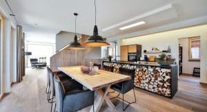 Einfamilienhaus Heidi mit offener Wohnküche, Kochinsel mit integriertem Holzlager, Essbereich, Treppenaufgang mit holzverblendeter Seitenwand und Blick in die Abstell- bzw. Speisekammmer von Regnauer Fertighaus.