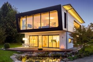 Einfamilienhaus Seebruck mit Flachdach, Panoramafenster im ersten Stock, überdachter Terrasse mit Schiebetüren, Holzdielenterrassenpodest und kleinem Biotop von Regnauer Fertighaus.