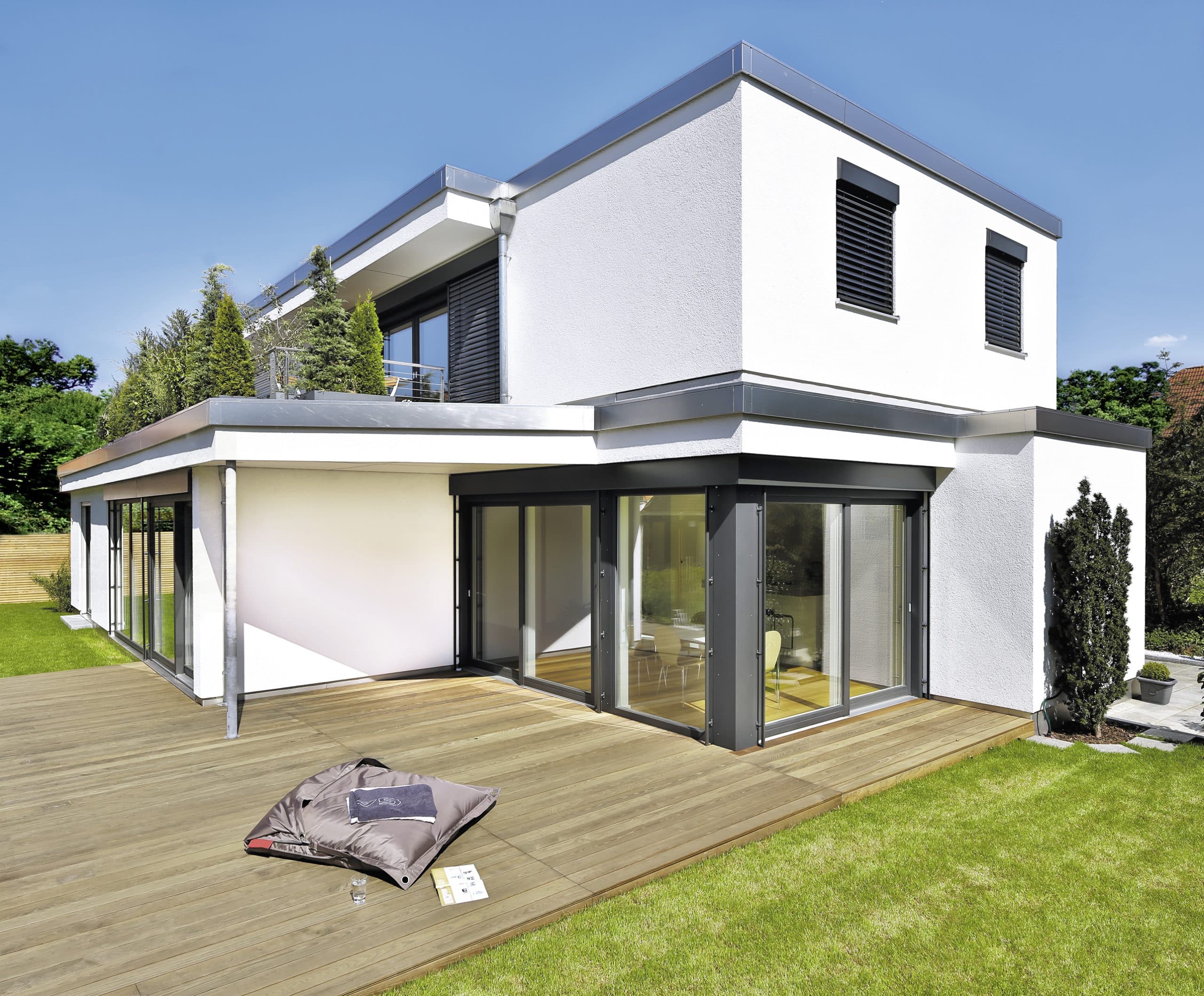 Einfamilienhaus mit Flachdach, halbüberdachter Eckterrasse mit Terrassenschiebetüren, zweitem Terrassenzugang, Holzdielenterrasse und einer Dachterrasse im Obergeschoß von Regnauer Fertighaus.
