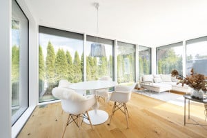 Regnauer Fertighaus zeigt großen hellen Wintergarten mit Eckcouch, Essbereich und raumhohen Fensterflächen mit Blick auf Terrasse und Garten.