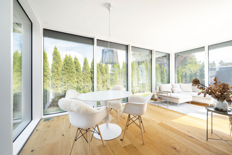 Regnauer Fertighaus zeigt großen hellen Wintergarten mit Eckcouch, Essbereich und raumhohen Fensterflächen mit Blick auf Terrasse und Garten.