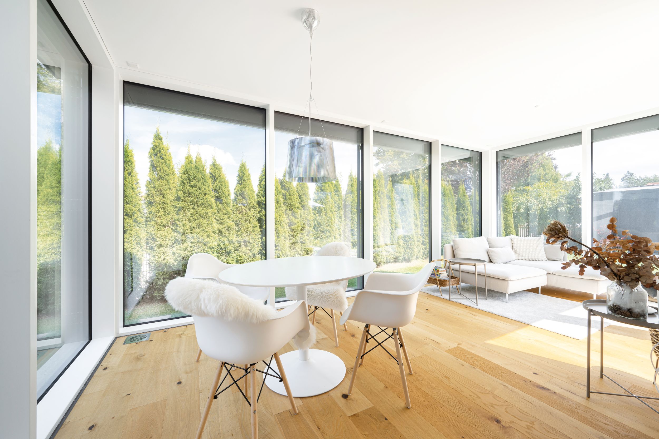 Regnauer Fertighaus zeigt großen hellen Wintergarten mit Eckcouch, Essbereich und raumhohen Fensterflächen mit Blick auf Terrasse und Garten.