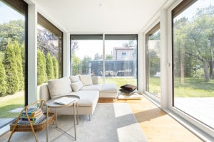 Regnauer Fertighaus zeigt Wintergarten mit Eckcouch und Glasschiebetüre mit Blick auf Terrasse und Garten.