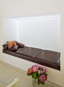 Ein Sitzfenster mit weißer Innenjalousie und gepolsterter, dunkelbrauner Ledersitzfläche von Regnauer.