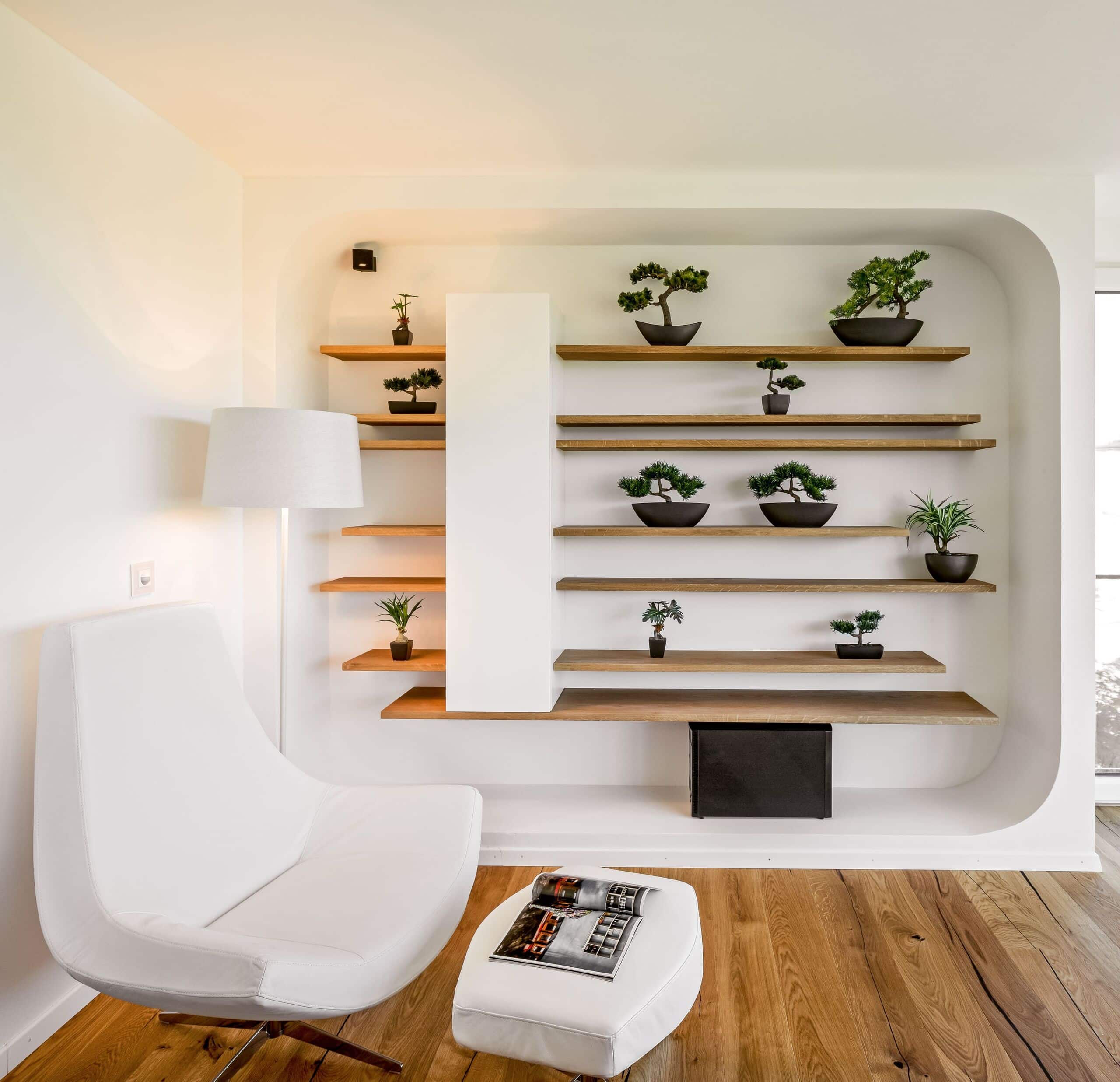 Zen bzw. den ulimativen Ruhepool erreicht man mit dieser Leseecke mit Loungsessel und passendem Schemel in Weiss, Stehleuchte und einem gemauerten Wandregal mit schwebenden Holzregalen und Bonsais von Regnauer.