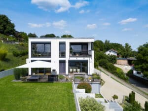 Eine moderne Flachdach‑Villa mit grosser Terrasse, gepflegtem Rasen und zwei französischen sowie einem regulären Balkon von Regnauer Hausbau.