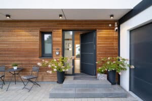 Ein überdachter Hauseingang mit Holzfassade, Außenspots und angrenzender Garage in einem Fertighaus von Regnauer Hausbau.