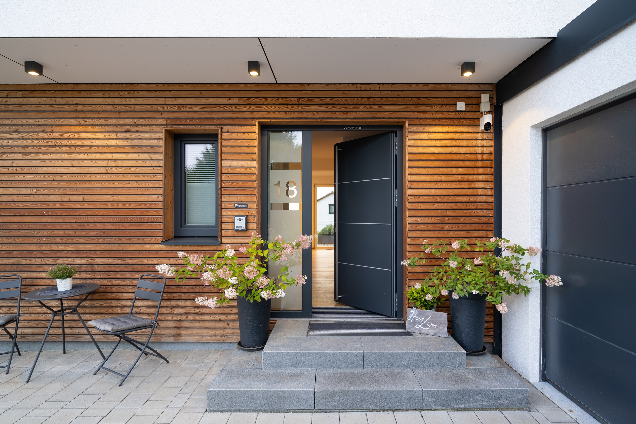 Ein überdachter Hauseingang mit Holzfassade, Außenspots und angrenzender Garage in einem Fertighaus von Regnauer Hausbau.
