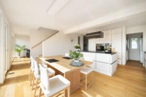 Ein offene Wohnküche und Essbereich mit grossen Terrassentüren, Blick zum Wohnbereich und elegantem Treppenaufgang von Regnauer Hausbau.