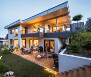 Ein modernes mehrstöckiges Haus mit Flachdach, Balkon mit Glas- und Holzelementen, großzügigen Fenstern und stimmungsvollem Sonnenuntergang von Regnauer.