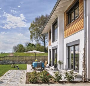 Ein modernes Einfamilienhaus mit Holzfassadenelementen, Dachüberstand, Terrassentüren mit schwarzem Alurahmen und gepflegtem, gepflastertem Außenbereich von Regnauer.