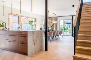 Eine modern-klassiche Wohnküche mit Kristallleuchten, Kücheninsel, Essbereich, hellen Holz-Alu-Terrassentüren und Holztreppe von Regnauer.