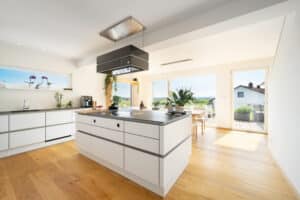 Eine moderne offene Wohnküche mit Kücheninsel, Essbereich und großen Fensterflächen von Regnauer.