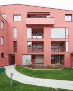 RÖFIX präsentiert die Außenansicht eines Mehrparteienhauses mit Satteldach, orangen Balkongeländern aus Metall und orangem Außenputz.