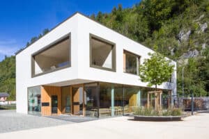 RÖFIX zeigt die Außenansicht eines Kindergartens mit Flachdach, Innenterrasse, Ganzglassystem und überdachtem Hauseingang.