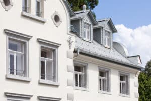 RÖFIX zeigt die Außenansicht einer renovierten Villa mit Satteldach und weißem Außenputz mit Verziehrungen.