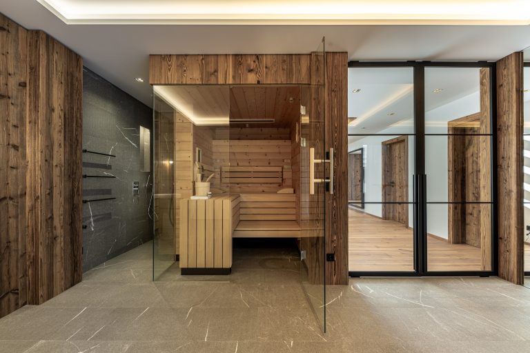 RUHA präsentiert eine Wellness-Raum mit kompakter Sauna aus dunklem Holz und einer barrierefreien Duschnische.