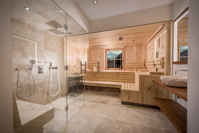 RUHA präsentiert einen Homespa-Raum mit großer Sauna aus hellem Holz, einer barrierefreien Dusche und einem Waschtisch mit aufgesetztem Waschbecken aus Stein.