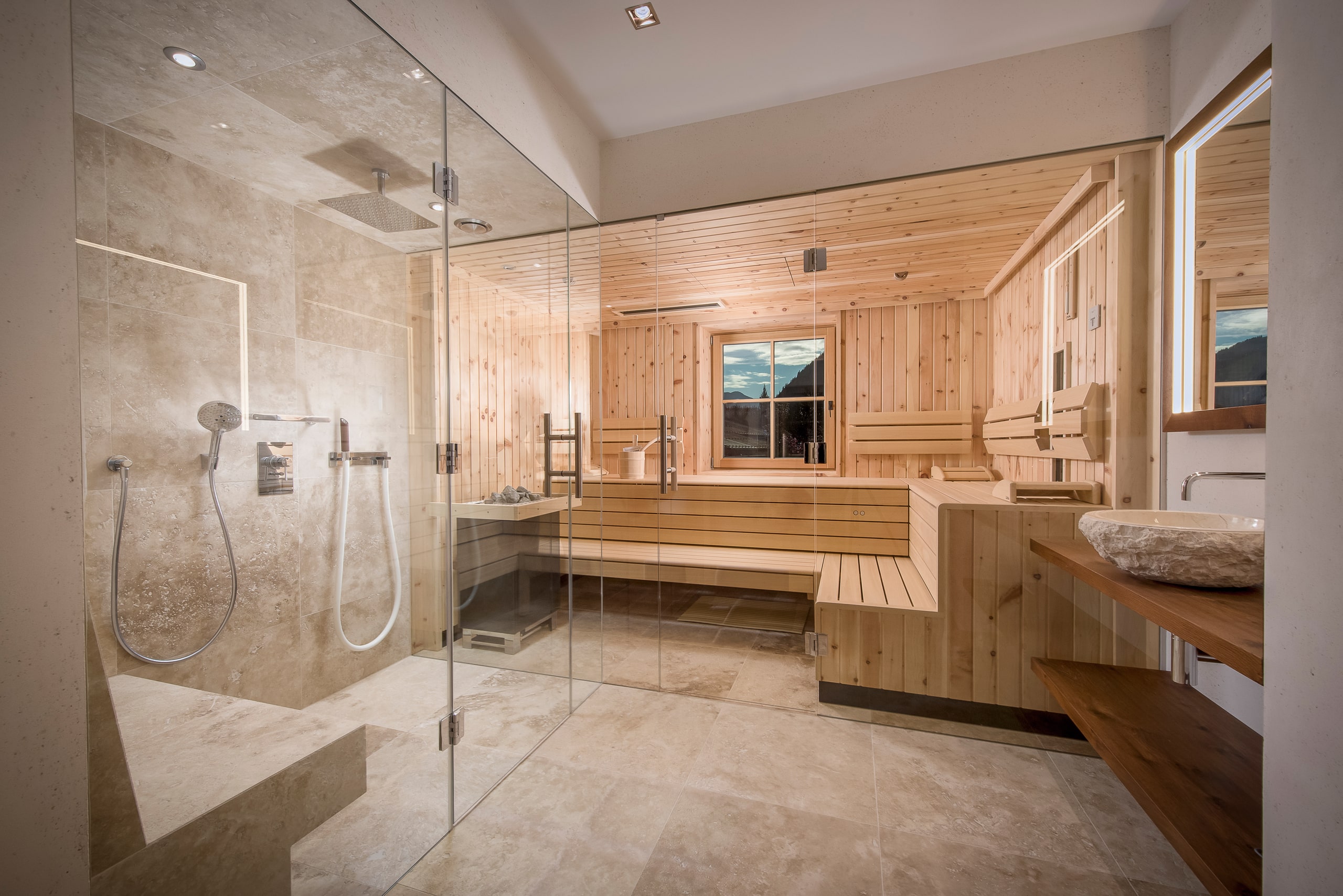 RUHA präsentiert einen Homespa-Raum mit großer Sauna aus hellem Holz, einer barrierefreien Dusche und einem Waschtisch mit aufgesetztem Waschbecken aus Stein.