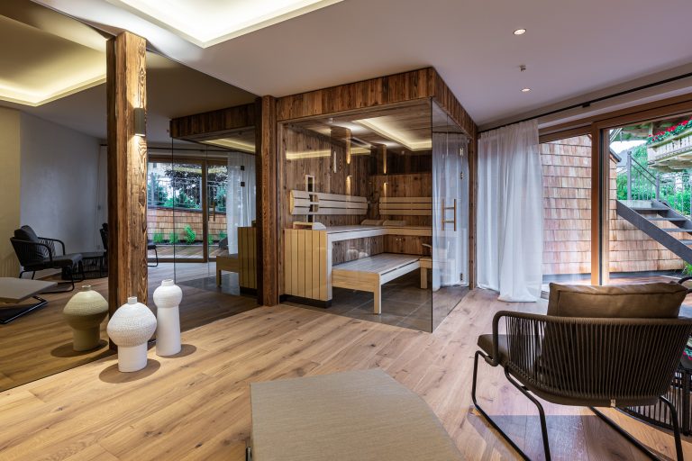 RUHA präsentiert einen Homespa-Raum mit großer Sauna aus Altholz, gemütlichen Stühlen und einem Zugang auf die Terrasse.