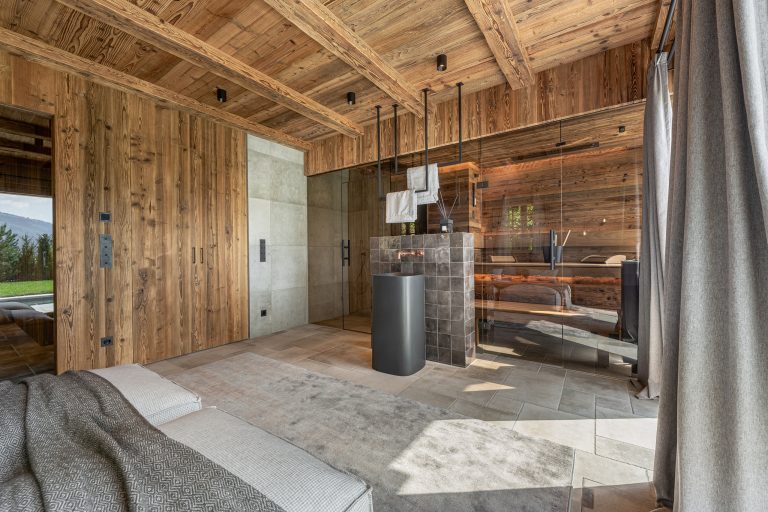 RUHA präsentiert einen Homespa-Raum mit großer Sauna aus Altholz, einen Waschbereich und einem Bett.