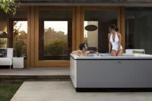 Ruha Stelzmüller zeigt ein Whirlpool mit einer grauen Außenhülle, das auf einer Terrasse vor einem modernen Haus im Freien steht.