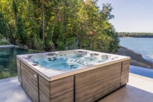 Ruha Stelzmüller zeigt ein Whirlpool mit vielen Düsen, das neben einem Pool steht und außen mit Holz verkleidet ist.