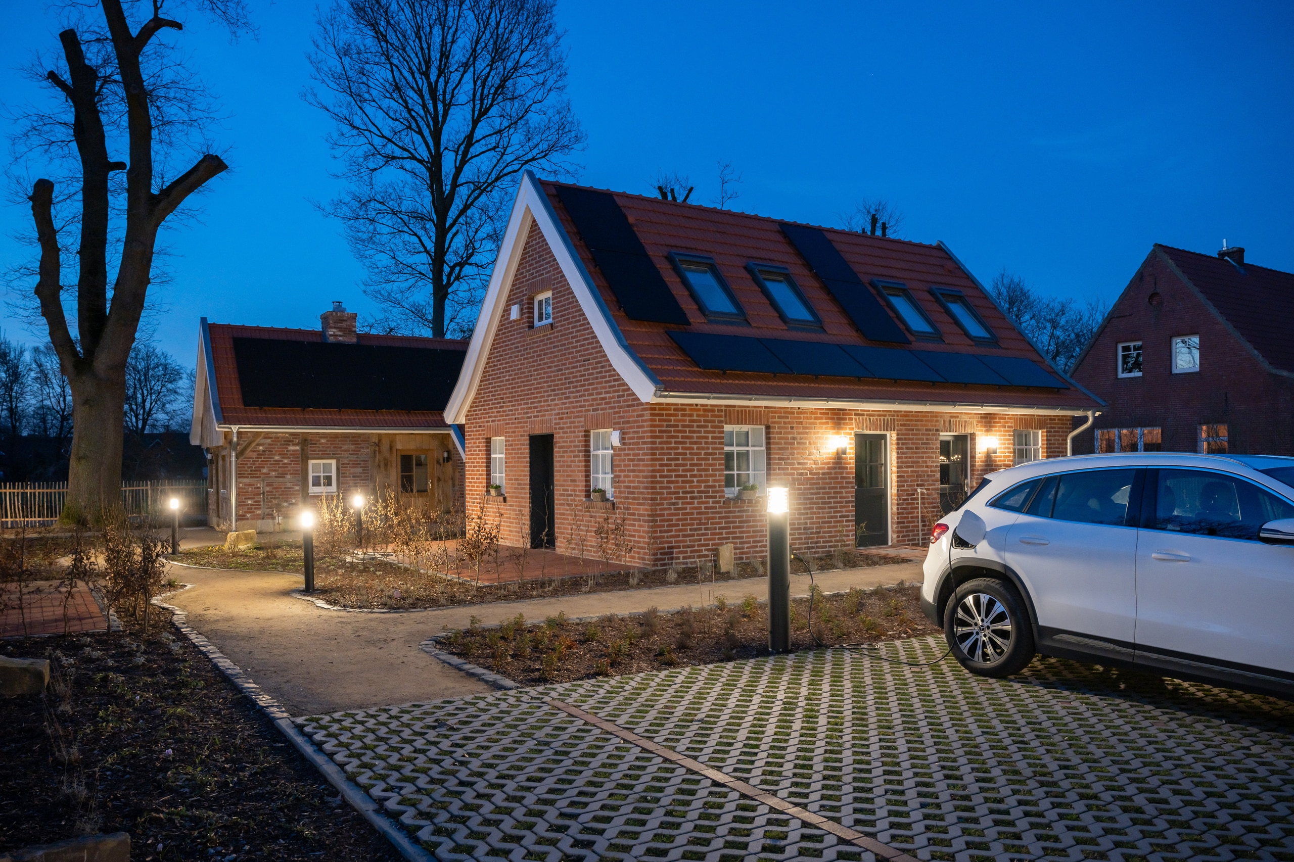 Ein Parkplatz in einer Wohnsiedlung mit Lichtsäule und integrierter Ladestation von RZB Energy, an der ein Elektroauto angeschlossen ist.