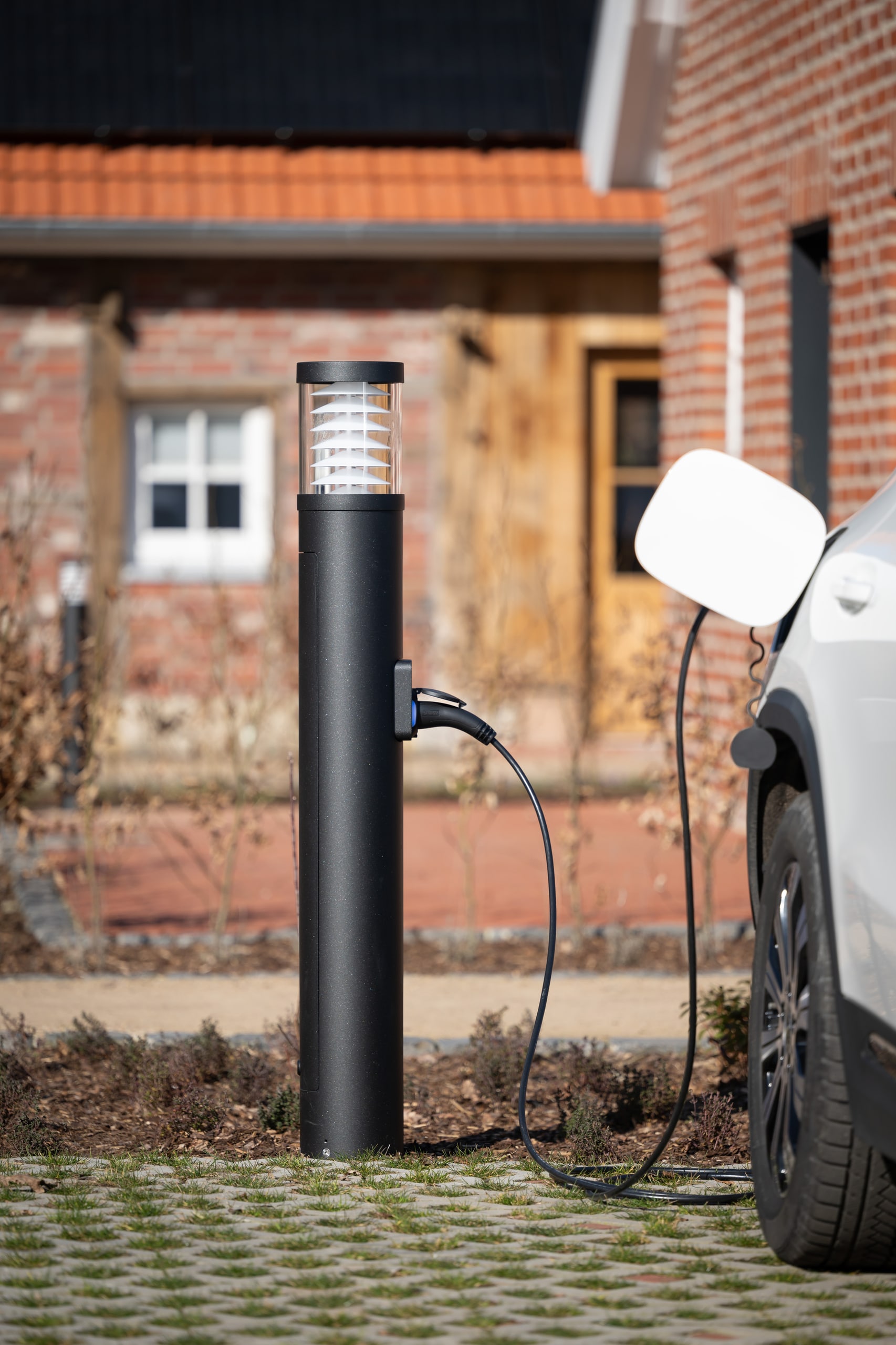 Ein Parkplatz mit Lichtsäule und integrierter Ladestation von RZB Energy, an der ein Elektroauto angeschlossen ist.