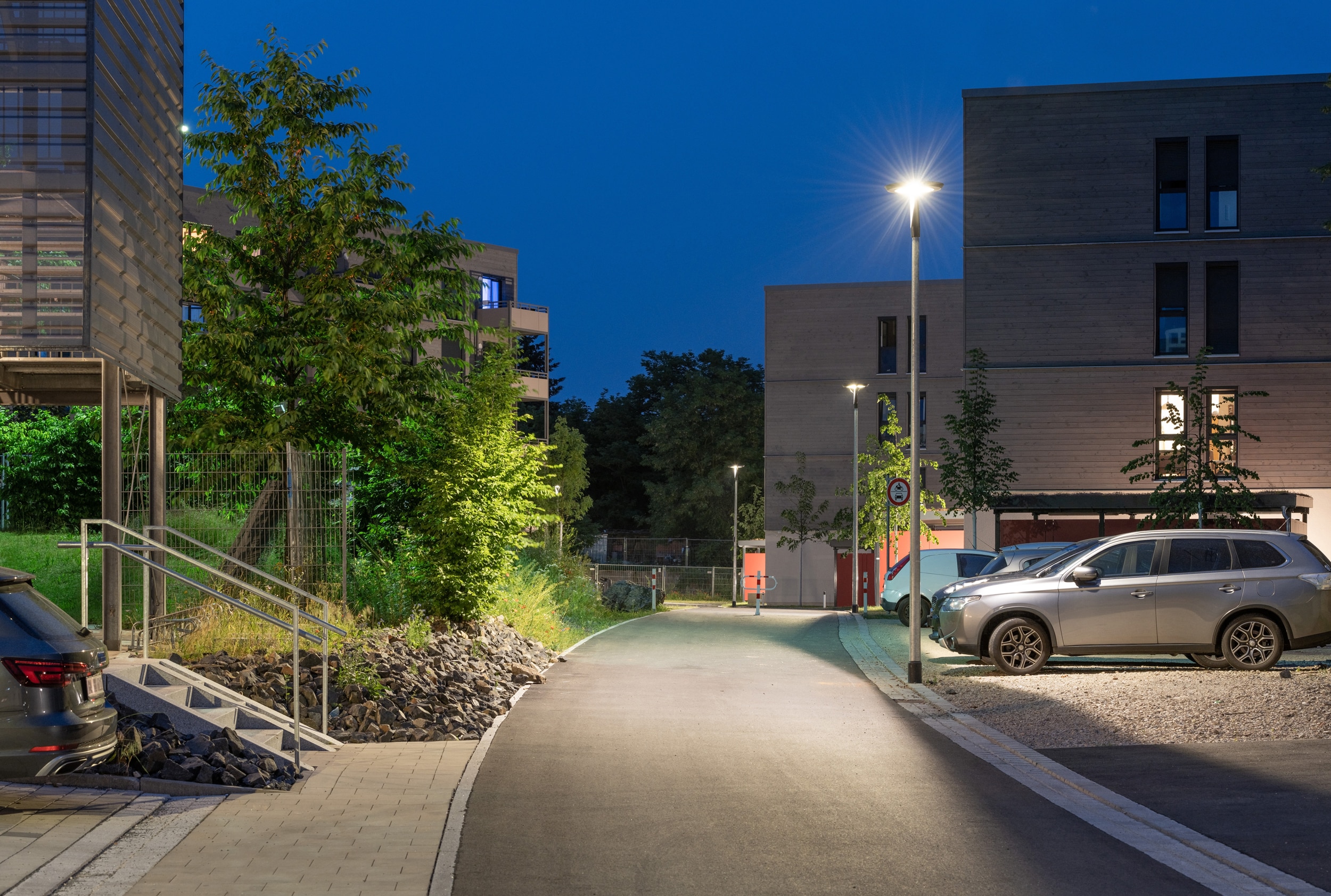 Straßenleuchten von RZB Energy erhellen sowohl Parkplatz als auch den Gehweg in einer Wohnsiedlung.