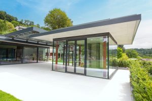 Mehrere auf einer Platform miteinander durch ein gemeinsames Flachdach verknüpfte Gebäude mit Fixverglasung, Glastüren und Hebeschiebetüren mit Alurahmen in Anthrazit von SCE Reisinger Bau.