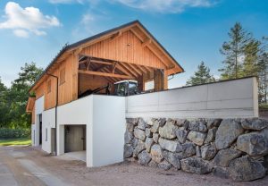 Heizhaus mit Sattel- und Pultdach, Fassadenmix aus Holz und Putz, zwei Garagen-Sektionaltoren, Hackgutlager und Schuppen für Landwirtschaftsgeräte von SCE Reisinger Bau.