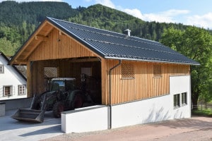Heizhaus mit Sattel- und Pultdach, Fassadenmix aus Holz und Putz, Hackgutlager und Schuppen für Landwirtschaftsgeräte mit Holzgitterfenstern von SCE Reisinger Bau von SCE Reisinger Bau.