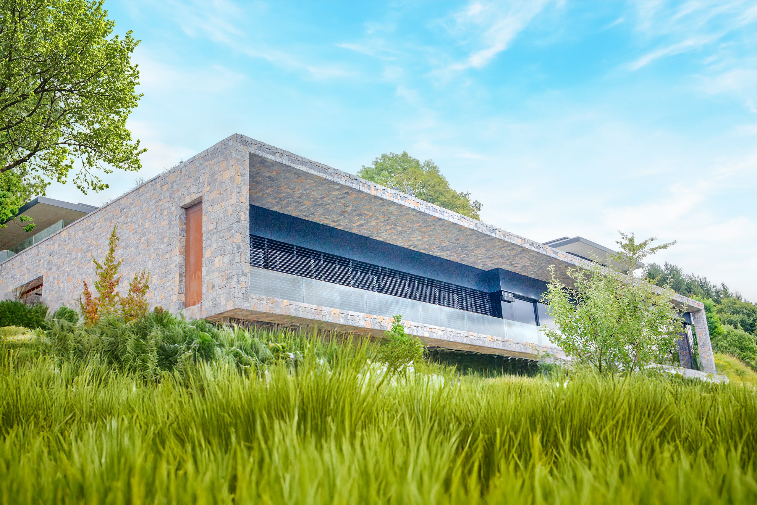Hanggebaute Villa mit Steinfassade, Flachdach und großzügiger Terrassenfront mit Glasgeländer von SCE Reisinger Bau.