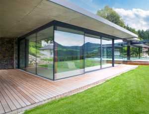 Flachdachgebäude mit Vollverglasung, Hebeschiebetüren, überdachter Terrasse und Terrassendielen von SCE Reisinger Bau.