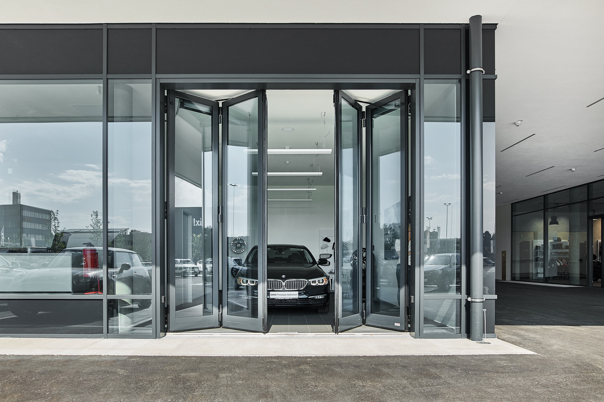 SCHNEIDER Torsysteme zeigt ein Autohaus mit einem gewerblichen voll-verglasten Falttore in anthrazit von außen, das gerade geöffnet wird.