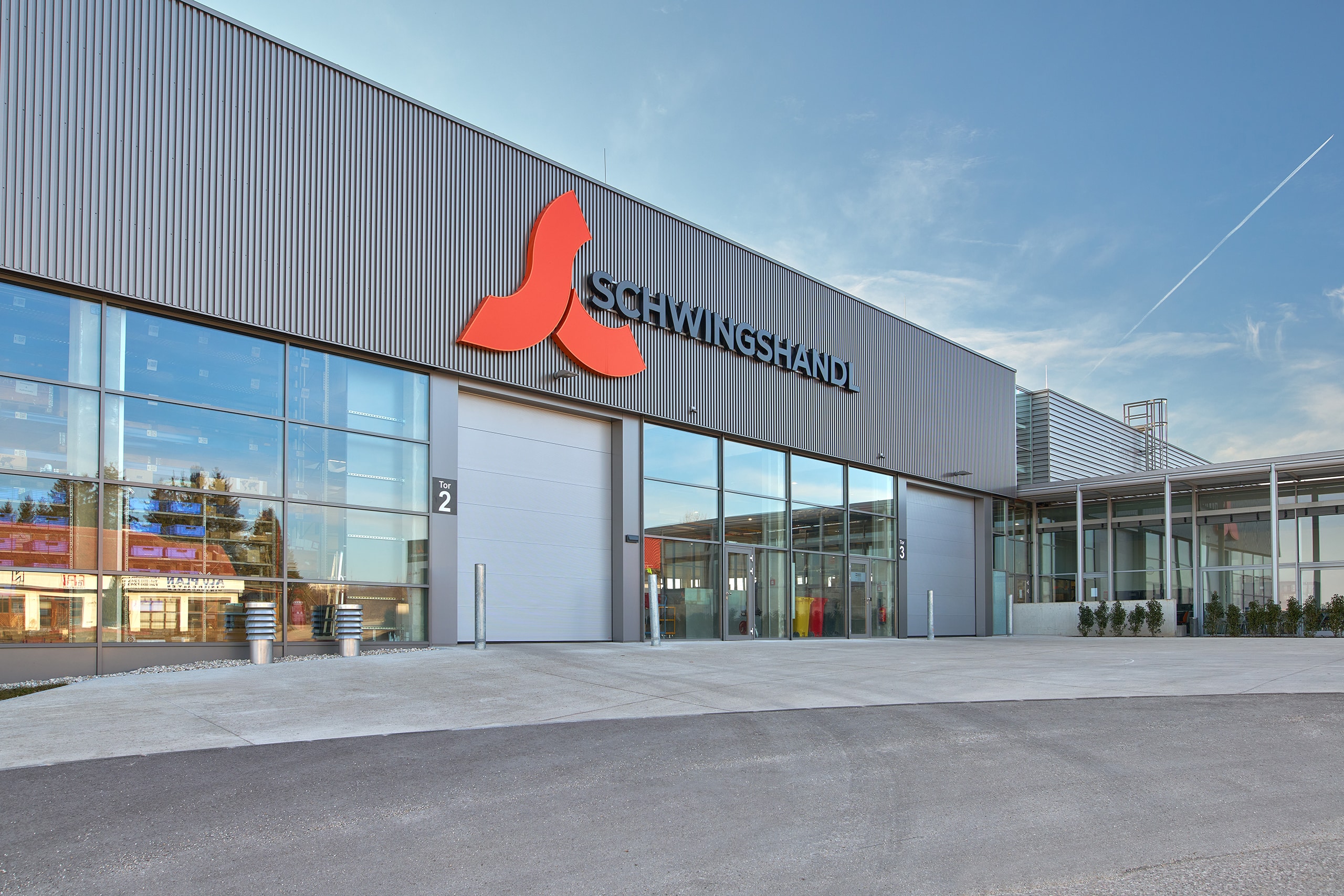 SCHNEIDER Torsysteme zeigt ein modernes Industriegebäude mit zwei geschlossenen gewerblichen Deckelsektionaltoren in hellgrau.