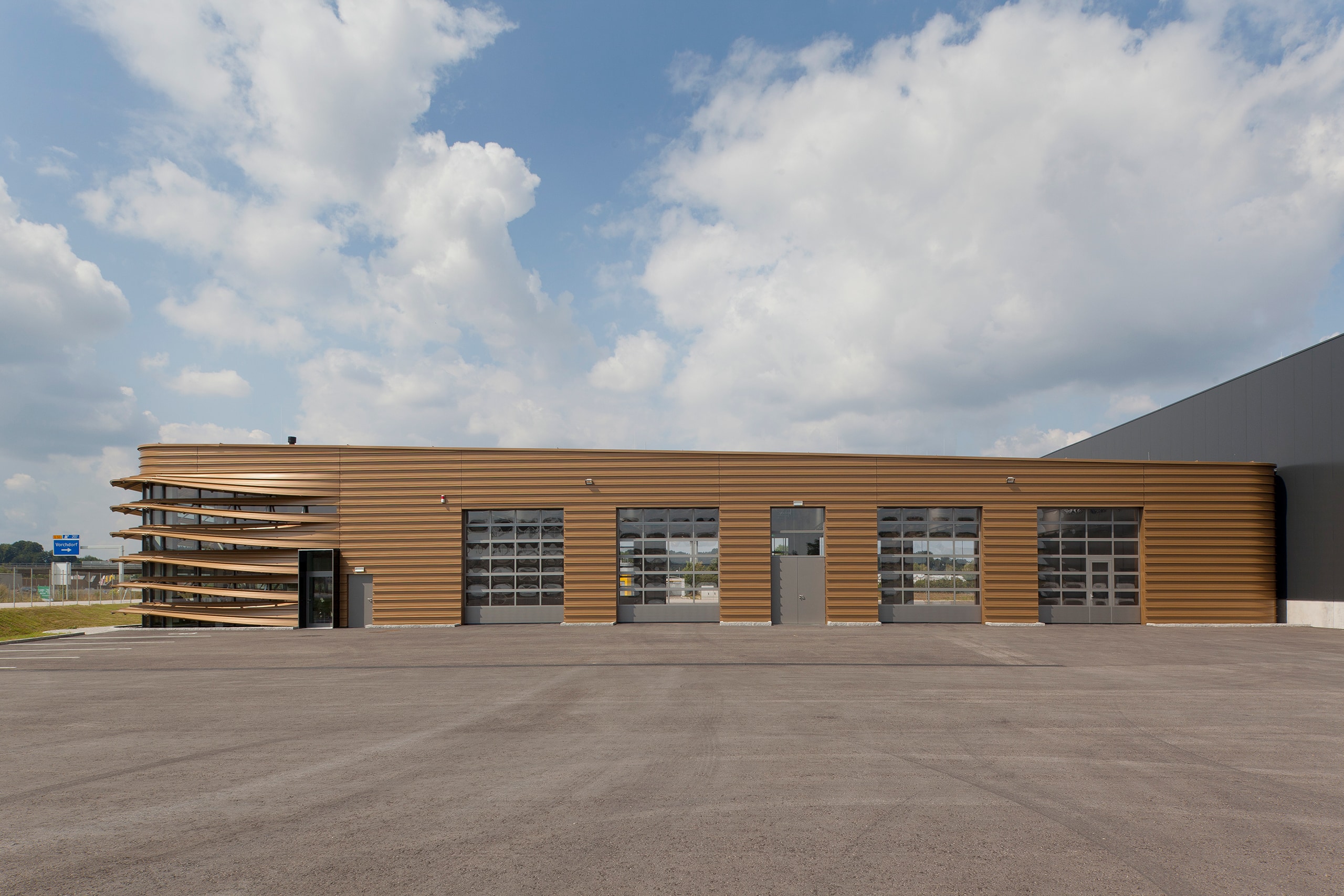 SCHNEIDER Torsysteme zeigt ein modernes Industriegebäude mit vier gewerblichen Deckelsektionaltoren in hellgrau mit teils eingebauter Türe.