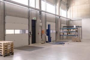 SCHNEIDER Torsysteme zeigt eine Industriehalle von innen mit einem gewerblichen Deckelsektionaltor in hellgrau mit eingebauten Fenstern.