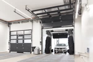 SCHNEIDER Torsysteme zeigt ein gewerbliches Deckensektionaltor einer Waschanlage mit Verglasung im oberen Teil und geschlossenen Elementen im unteren Teil mit integrierter Türe, das gerade geöffnet wird.