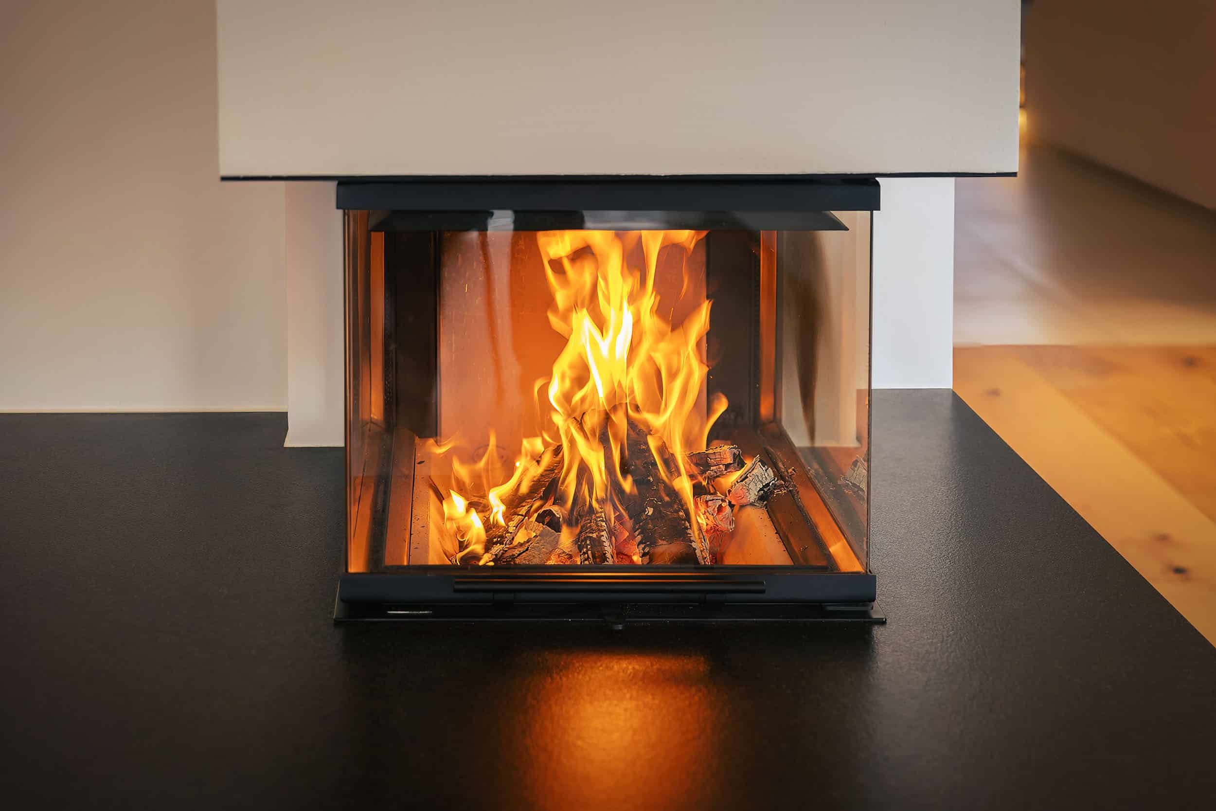Ein moderner Kamin mit schwarzem Feuertisch und dreiseitigem Sichtfenster in der Frontalansicht von Uwe Seidl Ofenbau.