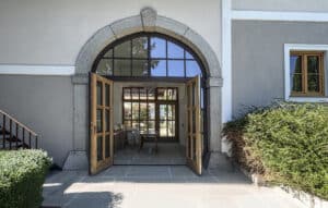 Altbau mit offenem zweiflügeligen Eingangstor mit Holzsprossen, einem Oberlicht mit Sprossen und Rundbogen sowie Seitenlichtern in - auf der Aussenseite - dunkellackiertem Holz von SILBER Fensterbau.