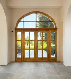 Innenaufnahme eines Altbaus mit imposantem zweiflügeligen Eingangstor mit Holzsprossen, einem Oberlicht mit Sprossen und Rundbogen sowie Seitenlichtern aus naturbelassenem Holz von SILBER Fensterbau.