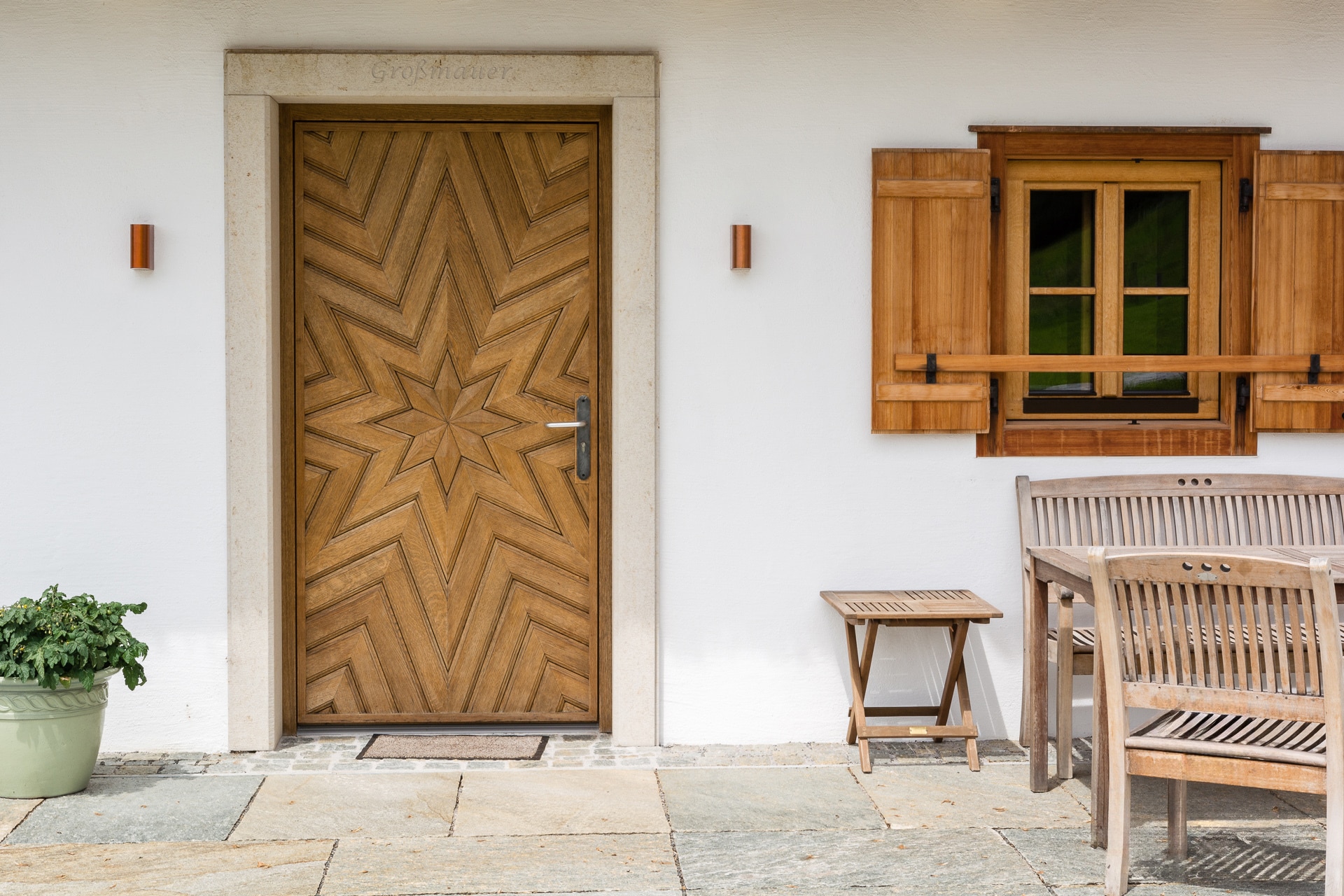 Rustikales Holzhaus im Landhausstil mit klassischen Holzsprossenfenstern mit Fensterläden und einer Hauseingangstüre in Vollholz mit kunstvollem Sternenmuster von SILBER Fensterbau.