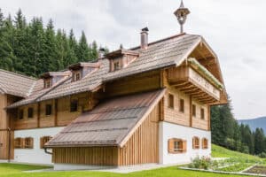 Rustikales Holzhaus mit klassischen Holzsprossenfenstern mit Fensterläden, Walmdach, Walmgauben, Schornsteinen und einem Holzbalkon von SILBER Fensterbau.