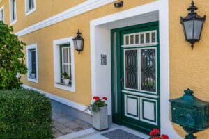 Klassische Villa bzw. Gutshaus mit gelber Fassade, weissen Akzenten, Holzsprossenfenster und einer Hauseingangstüre mit verspielten Glaselementen, beides in dunkelgrünem und weiss-lackierten Holz von SILBER Fensterbau.