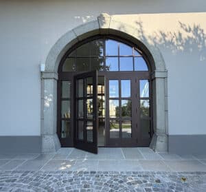 Altbau mit zweiflügeligen Eingangstor mit Holzsprossen, einem Oberlicht mit Sprossen und Rundbogen sowie Seitenlichtern, dunkel lackiert von SILBER Fensterbau.