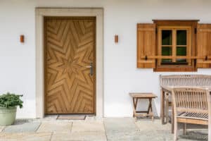 Rustikales Holzhaus im Landhausstil mit klassischen Holzsprossenfenstern mit Fensterläden und einer Hauseingangstüre in Vollholz mit kunstvollem Sternenmuster von SILBER Fensterbau.